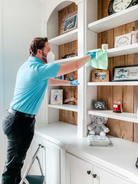 cleaning professional deep cleaning a bedroom by dusting high shelves with a step stool