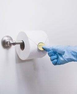 Maid wearing a blue glove and placing a gold Merry Maids seal on a neatly folded toilet paper roll